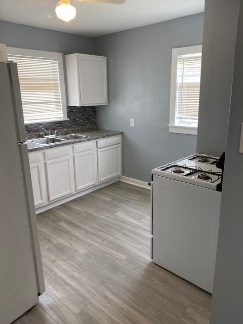 kitchen with white appliances, white cabinets, sink, decorative backsplash, and light wood-type flooring