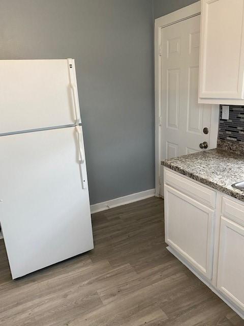 kitchen featuring white cabinets, white refrigerator, decorative backsplash, light stone countertops, and wood-type flooring