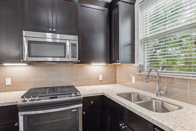 kitchen with light stone countertops, tasteful backsplash, dark brown cabinets, stainless steel appliances, and sink