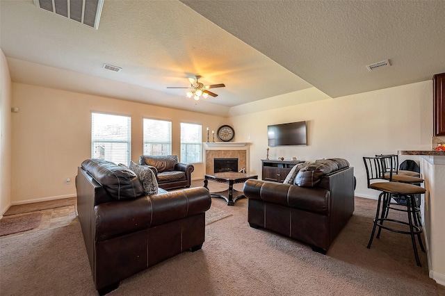 living room with a tiled fireplace, light carpet, ceiling fan, and a textured ceiling