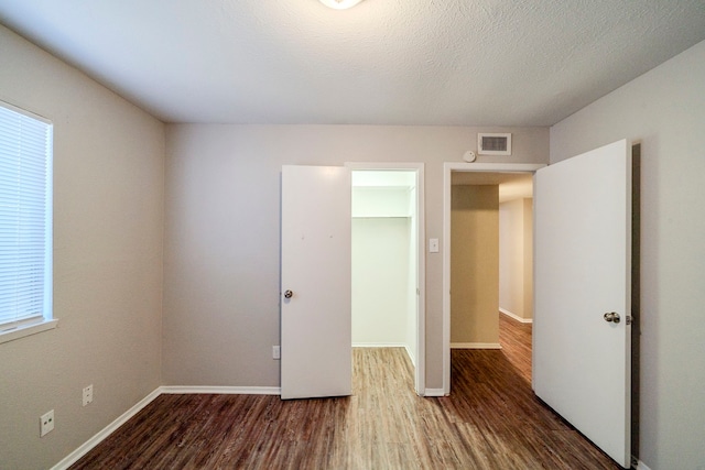 unfurnished bedroom with a textured ceiling, dark hardwood / wood-style flooring, a closet, and multiple windows