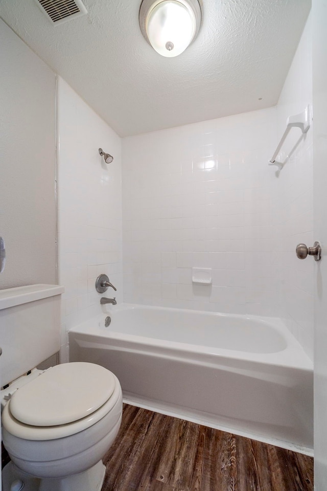 bathroom featuring tiled shower / bath combo, toilet, wood-type flooring, and a textured ceiling