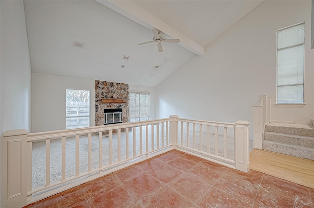 spare room with vaulted ceiling with beams, a stone fireplace, and ceiling fan