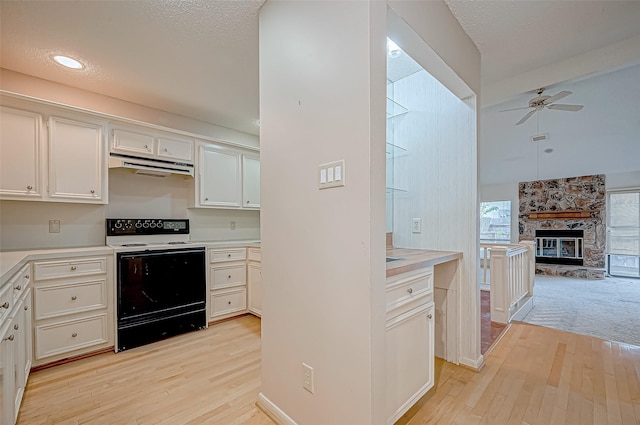 kitchen featuring white cabinetry, a stone fireplace, electric range, and light hardwood / wood-style flooring