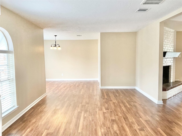 empty room with a textured ceiling, light hardwood / wood-style floors, a notable chandelier, and a brick fireplace