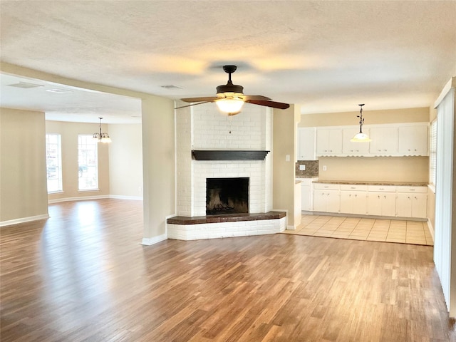 unfurnished living room with a fireplace, light wood-type flooring, a textured ceiling, and ceiling fan with notable chandelier