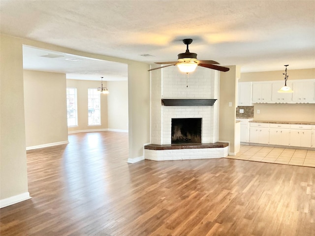 unfurnished living room featuring a textured ceiling, ceiling fan with notable chandelier, light wood-type flooring, and a fireplace