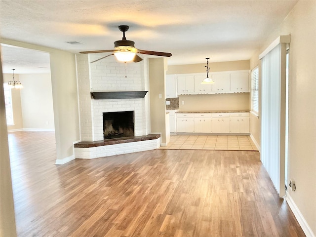 unfurnished living room with a textured ceiling, a fireplace, light hardwood / wood-style flooring, and ceiling fan with notable chandelier