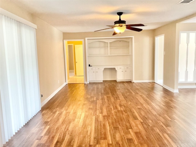 unfurnished living room featuring ceiling fan, built in features, built in desk, and light wood-type flooring