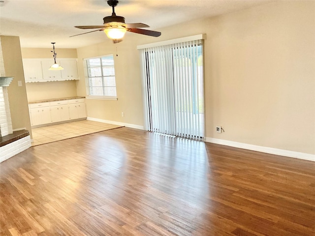 unfurnished living room with a brick fireplace, ceiling fan, and light hardwood / wood-style flooring