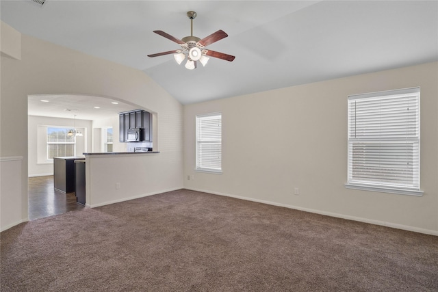 unfurnished living room with dark colored carpet, ceiling fan with notable chandelier, and lofted ceiling