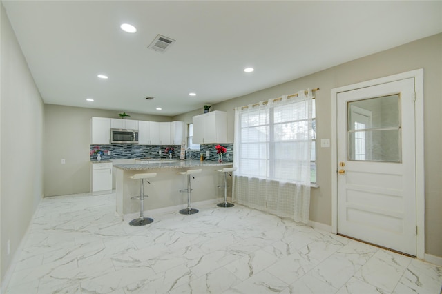 kitchen with white cabinets, a kitchen breakfast bar, decorative backsplash, light stone countertops, and kitchen peninsula