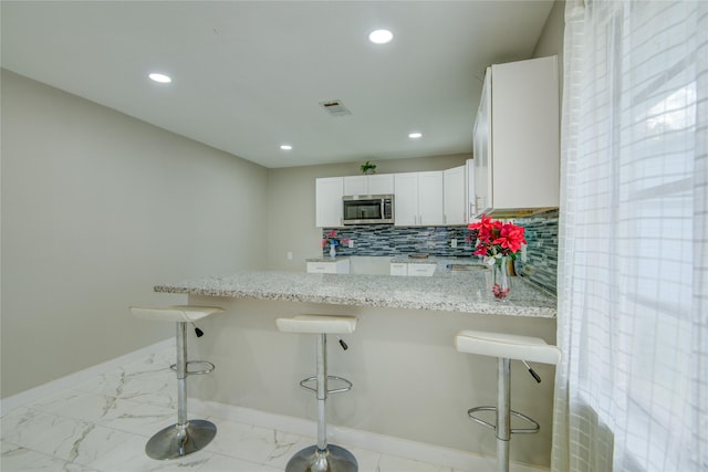 kitchen with light stone counters, kitchen peninsula, a breakfast bar area, decorative backsplash, and white cabinets