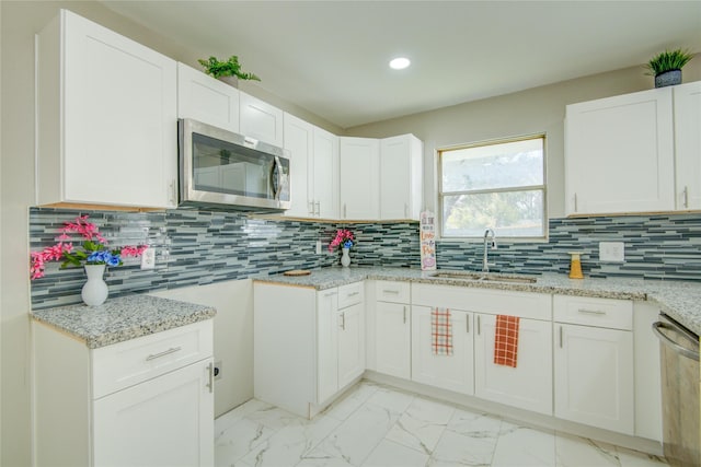 kitchen with white cabinets, sink, decorative backsplash, appliances with stainless steel finishes, and light stone counters