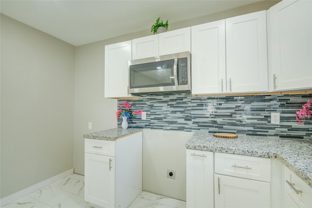 kitchen featuring white cabinets, light stone counters, and backsplash