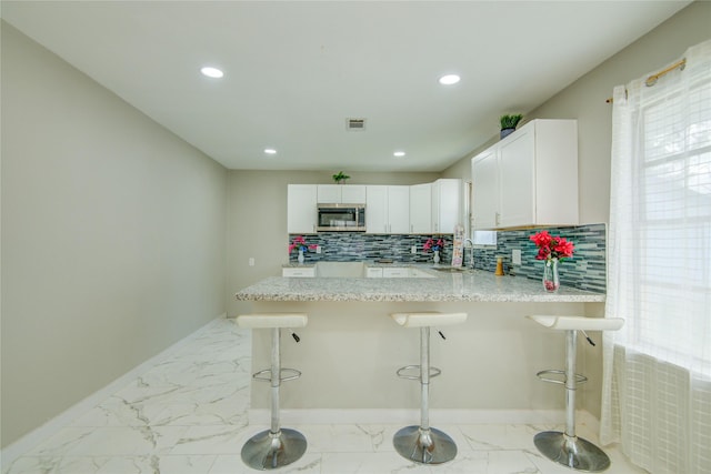 kitchen with white cabinets, a kitchen breakfast bar, kitchen peninsula, and sink