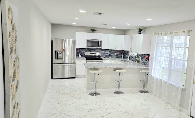 kitchen with a kitchen breakfast bar, sink, decorative backsplash, appliances with stainless steel finishes, and white cabinetry