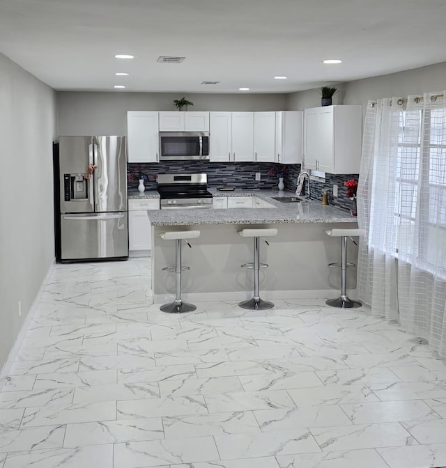 kitchen featuring a breakfast bar area, white cabinetry, light stone counters, kitchen peninsula, and stainless steel appliances