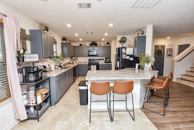 kitchen featuring a kitchen breakfast bar, light stone counters, a textured ceiling, gray cabinets, and black appliances