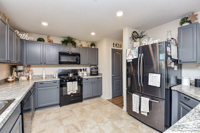 kitchen featuring black appliances, gray cabinetry, light stone countertops, and sink