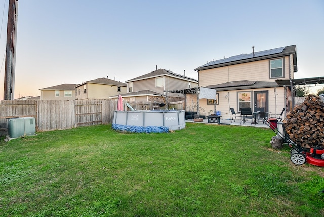 back house at dusk featuring a lawn, solar panels, a patio area, and a fenced in pool