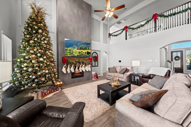 living room featuring ceiling fan, a fireplace, a towering ceiling, and hardwood / wood-style flooring