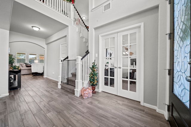 foyer entrance featuring arched walkways, french doors, visible vents, wood finished floors, and stairs