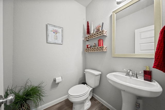 half bath featuring a sink, wood finished floors, toilet, and baseboards