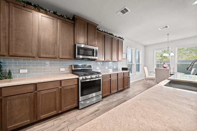 kitchen with visible vents, appliances with stainless steel finishes, wood tiled floor, light countertops, and backsplash