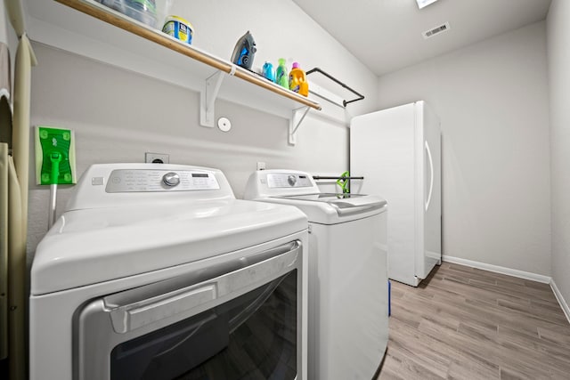 clothes washing area with washing machine and dryer, light wood-style flooring, laundry area, visible vents, and baseboards