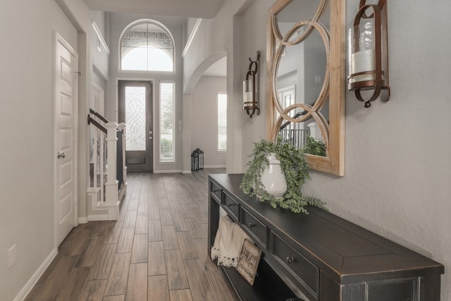 foyer entrance featuring arched walkways, baseboards, and wood tiled floor