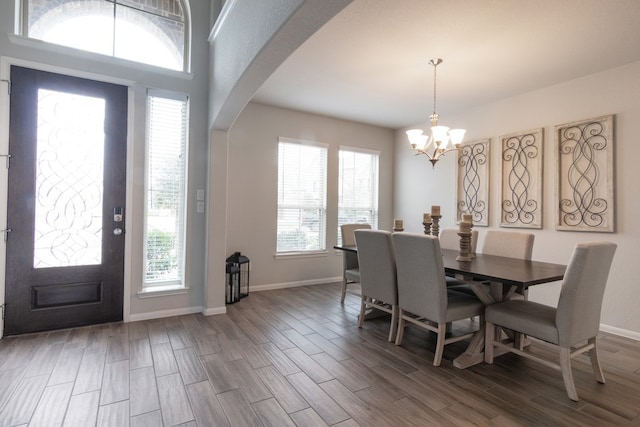 dining area with arched walkways, dark wood-style flooring, an inviting chandelier, and baseboards