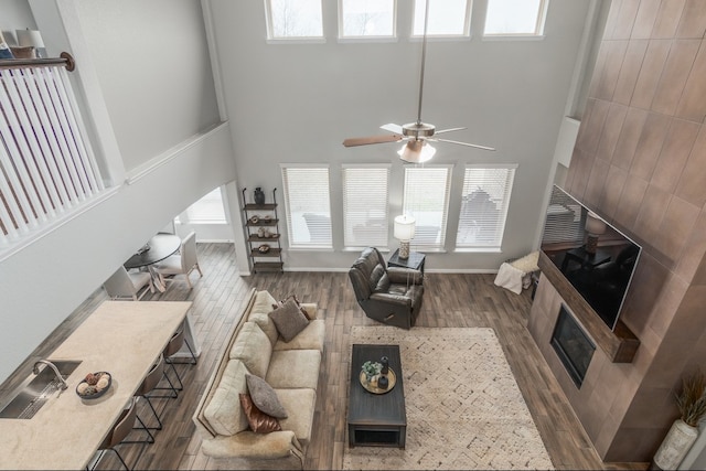 living area featuring baseboards, arched walkways, ceiling fan, wood finished floors, and a high ceiling