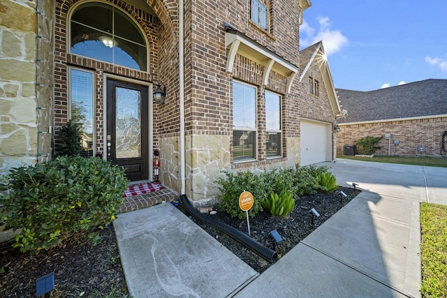 doorway to property featuring driveway, brick siding, an attached garage, and stone siding