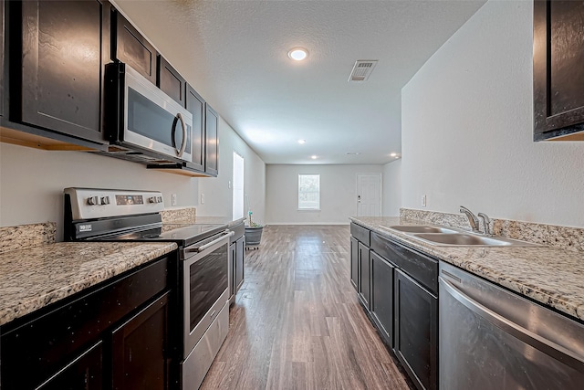 kitchen featuring dark brown cabinetry, light stone countertops, sink, stainless steel appliances, and light hardwood / wood-style flooring