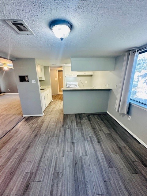 kitchen with kitchen peninsula, a textured ceiling, white cabinetry, and dark wood-type flooring