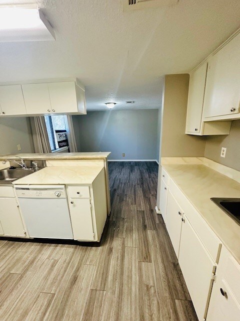 kitchen featuring kitchen peninsula, white cabinetry, dishwasher, and light wood-type flooring