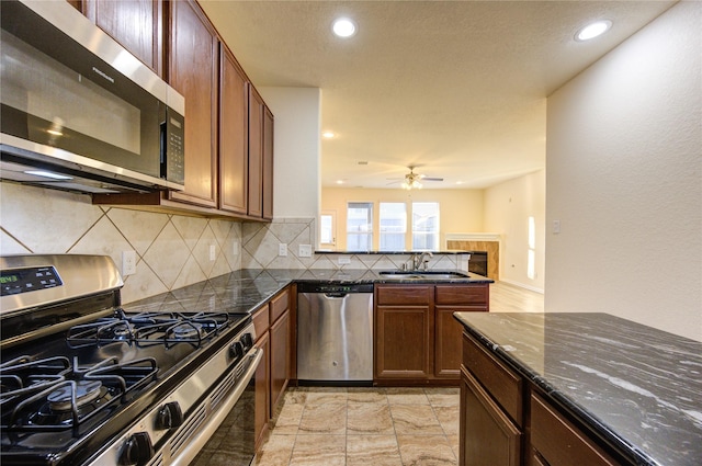 kitchen with ceiling fan, sink, backsplash, dark stone counters, and appliances with stainless steel finishes