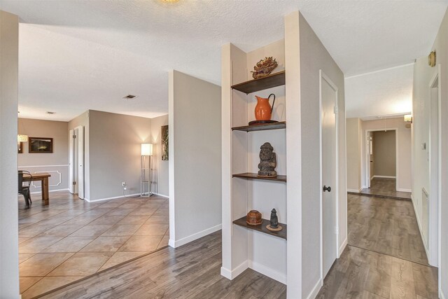 corridor with built in features, a textured ceiling, and hardwood / wood-style flooring