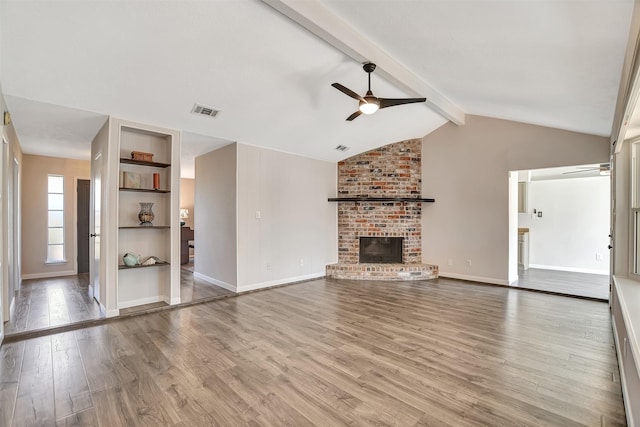 unfurnished living room featuring a brick fireplace, ceiling fan, lofted ceiling with beams, and light wood-type flooring