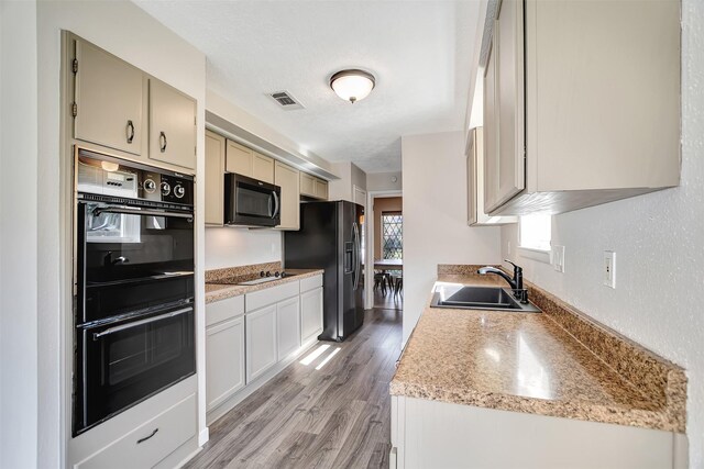 kitchen with sink, light stone counters, light hardwood / wood-style flooring, a textured ceiling, and black appliances