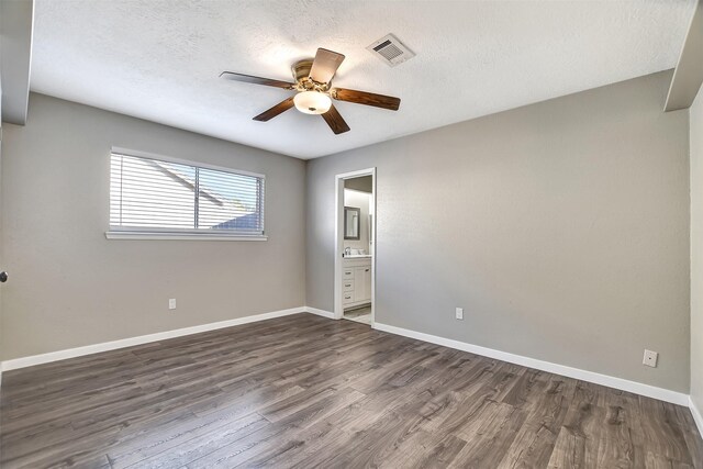 unfurnished bedroom with ceiling fan, dark hardwood / wood-style flooring, a textured ceiling, and connected bathroom