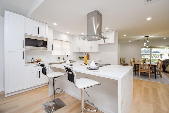 kitchen with island range hood, stainless steel microwave, white cabinets, and light wood-type flooring