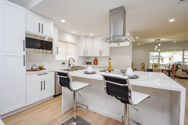 kitchen featuring island range hood, white cabinetry, appliances with stainless steel finishes, and light hardwood / wood-style flooring