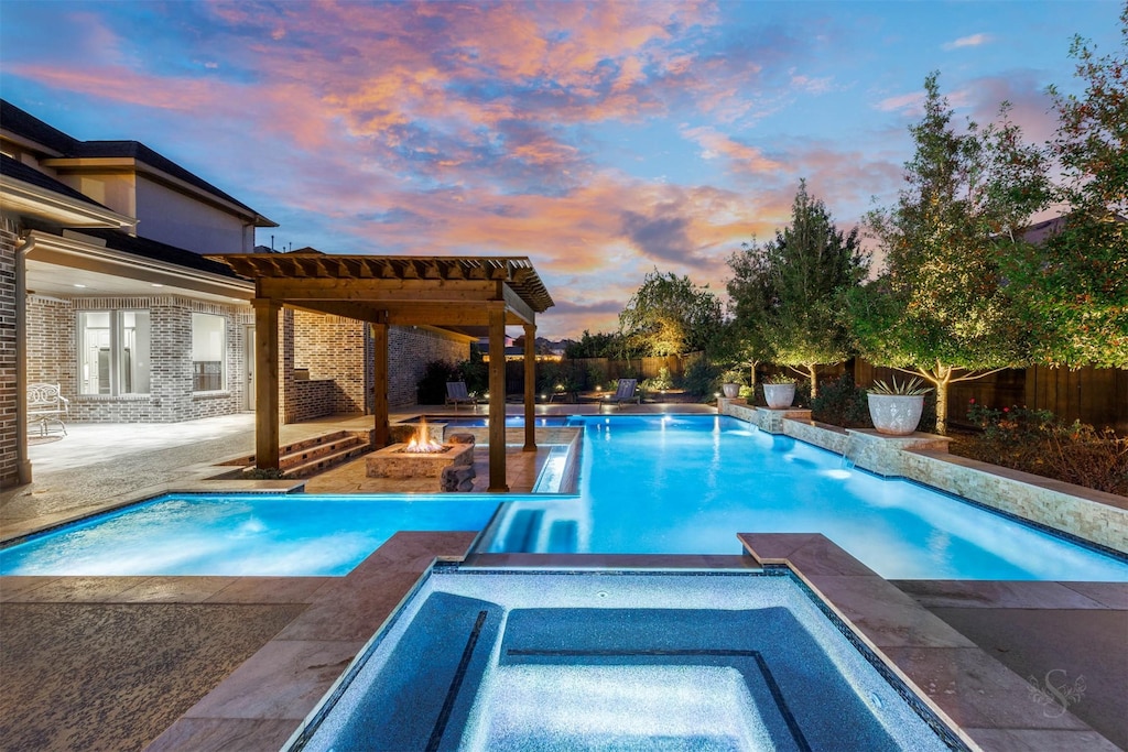 pool at dusk with a fire pit and an in ground hot tub