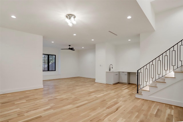 unfurnished living room featuring light wood-type flooring, ceiling fan, and sink