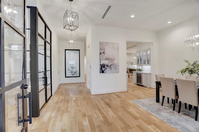 foyer entrance with a notable chandelier, light hardwood / wood-style floors, and beverage cooler