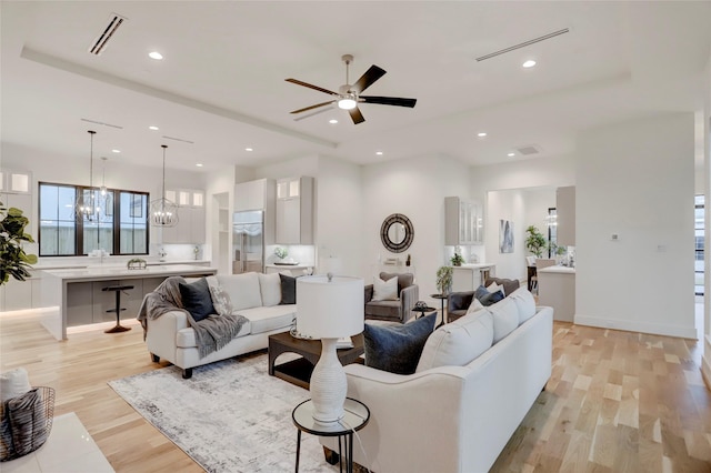 living room featuring ceiling fan with notable chandelier and light wood-type flooring