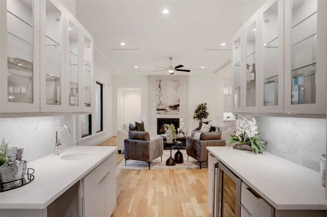 kitchen featuring light wood-type flooring, backsplash, beverage cooler, sink, and a fireplace