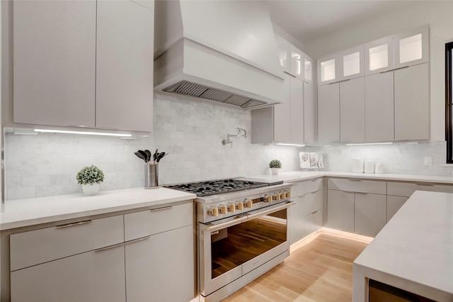 kitchen with premium range hood, white cabinets, light hardwood / wood-style flooring, decorative backsplash, and stainless steel range